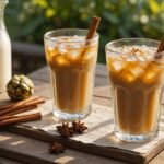 Golden iced chai in tall glass with ice cubes, cardamom pods and cinnamon sticks on wooden table, af
